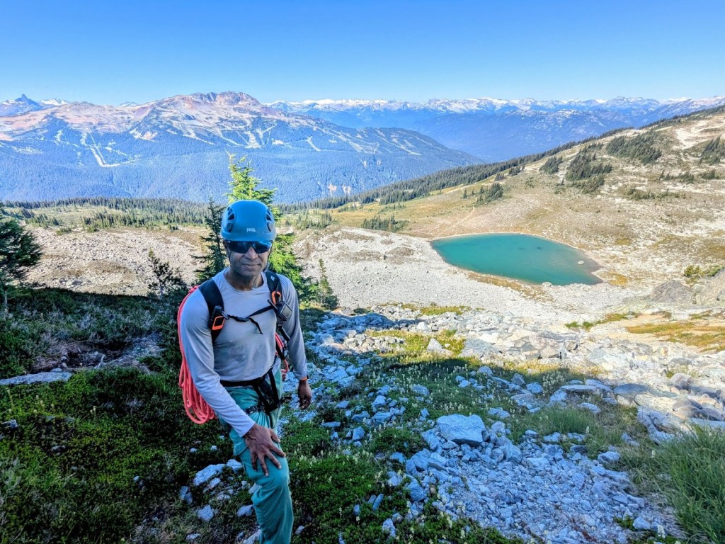 Scramble up the base of the DOA buttress, Blackcomb lake in the background, Shashi carrying the rope.